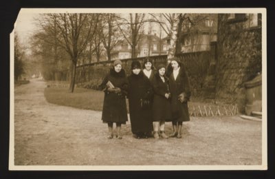 Front shows a group of five women standing together in a park or garden path with bare trees and a stone wall in the background. Winter clothing. If the mother was 45 in January 1931, she was born approximately 1885-1886.