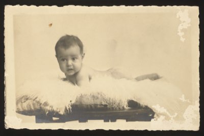 Front shows a baby lying on a fur rug on a small bench/table, approximately 5 months old.