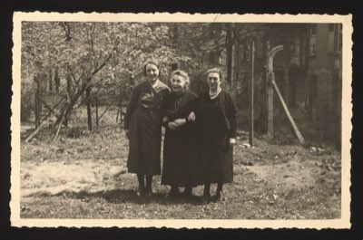 Front shows three elderly women standing together in a garden/courtyard with trees and buildings in the background. One of them is identified as 