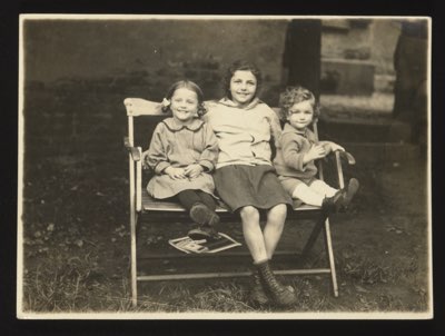 Front shows three children sitting on a garden bench — two girls and a boy (or toddler). The playful title 