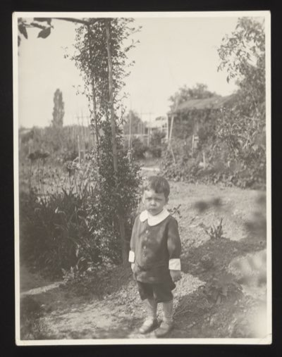 Front (0014) shows a small boy standing in a garden path with flowers and a greenhouse in the background. Same child as photo 0012/0013 (Walter), June 1930.
